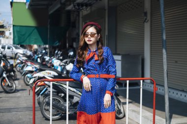 Markette kırmızı barikata yaslanmış mavi ve kırmızı retro elbiseli, dalgalı esmer kadın..