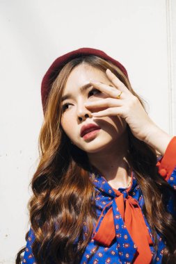 Mavi ve kırmızı retro elbiseli, dalgalı esmer kadının beyaz duvardaki bir süpermodel gibi yüzüne dokunuşunu yakından çek..