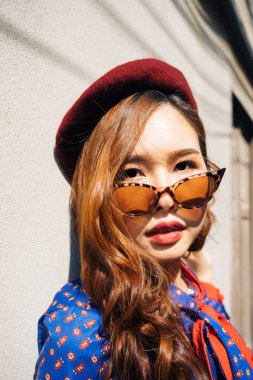 Dalgalı esmer, mavi ve kırmızı retro elbiseli kadının güneş ışığında beyaz duvarda dikilirkenki yakın çekimi..