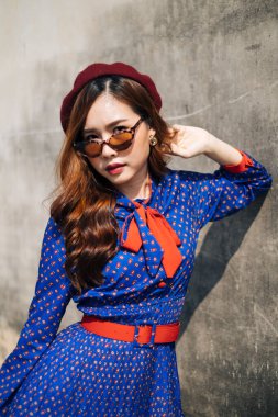 Mavi ve kırmızı retro elbiseli esmer kadının portresi. Eski duvarda havalı bir duruşu var. Yaklaş..