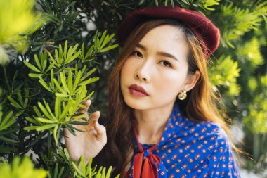 Yeşil yaprağın önünde duran mavi ve kırmızı retro elbiseli esmer kadının portresi..