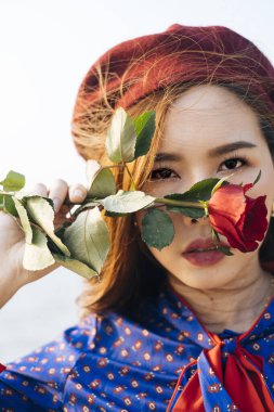 Dalgalı esmer, mavi ve kırmızı retro elbiseli kadını yakından çek. Yüzünü gülle gizle..