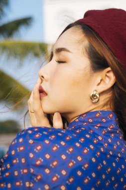 Dalgalı esmer, mavi ve kırmızı retro elbiseli kadının yakın plan çekimi. Güneş ışığında, dikey olarak ağzına dokun..