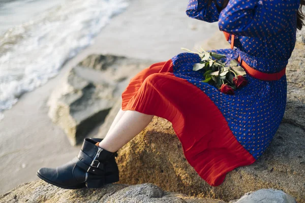 Cropped image of roses and woman\'s body sitting on the rock at the beach.