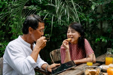 Asyalı yaşlı bir çift evlerinin arka bahçesinde kahvaltı yapıyor..