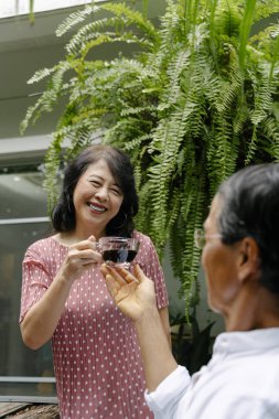 Yaşlı Asyalı kadın arka bahçede kocasına bir fincan kahve veriyor..