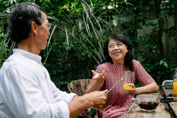 Yaşlı Asyalı çift bahçede kahvaltı ederken tablette dijital haber okuyor..