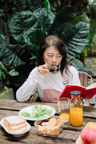 Mujer Mayor Bebiendo Café Leyendo Libro Jardín — Foto de Stock