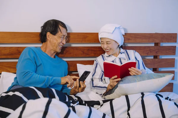 アジアの高齢者のカップルは スマートフォンでニュースを読んで 寝室で本を読む — ストック写真