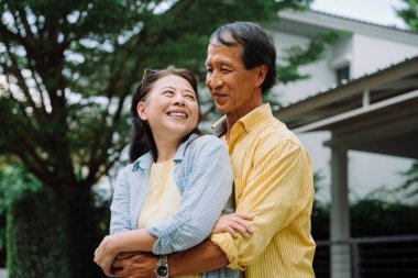 Arka bahçede kucaklaşan Asyalı yaşlı bir çiftin portresi..