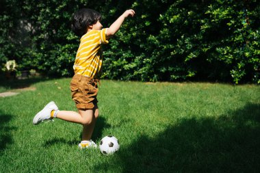 Parktaki yeşil alanda koşan ve futbol oynayan Asyalı çocuğun bacakları..