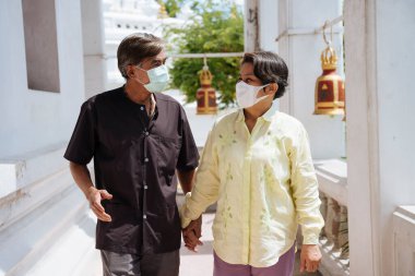 Romantik Asyalı yaşlı çift tapınakta yürürken maske takıyor..