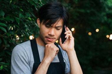 Asyalı düşünceli adam, avluda konuşurken siyah önlük giyiyor..