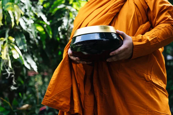 Monk in yellow robe holding a bowl for alms offering in the morning.