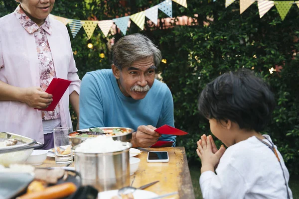 Grandfather giving red envelope to a youngest kid in the family in dining party outdoor.