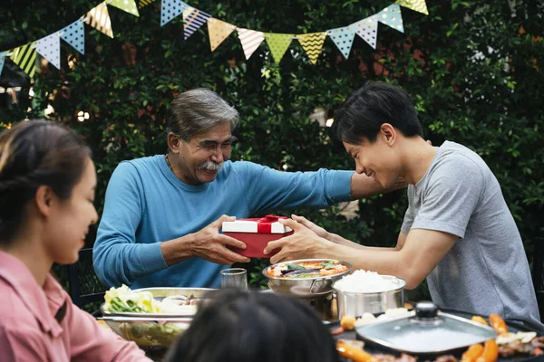 Asian son and father giving gift box in party outdoors.