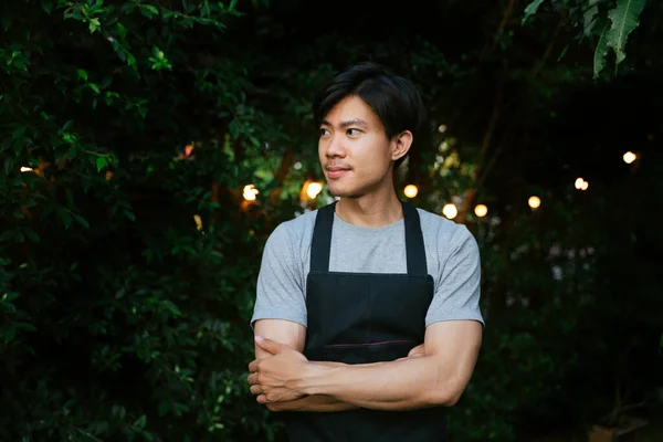 Portrait of cheerful asian waiter wear black apron at yard restaurant.