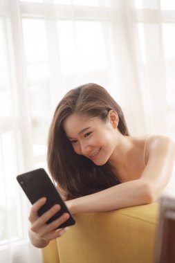 Kanepede akıllı telefon kullanan Asyalı genç bir kadının portresi..