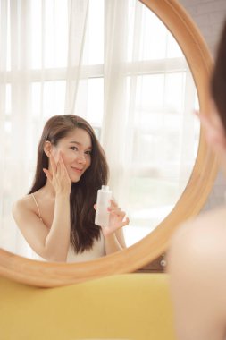 Genç Asyalı güzel kadın aynanın önünde yüz kremi kullanıyor. Cilt bakımı kavramı.