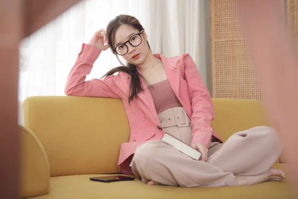 若いですアジアの美しさ女性着用ピンクジャケットと眼鏡上のソファにホーム — ストック写真