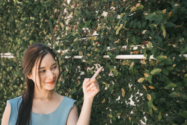 若いですアジアの美しさ女性Pointing指で空のスペース上の緑の葉壁 — ストック写真