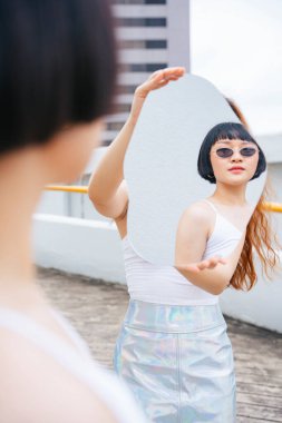 Genç Asyalı kısa saçlı kadın portresi aynaya bakarken güneş gözlüğü takıyor..