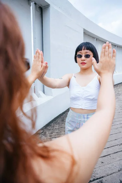 Portrait of young asian bob hairstyle in white vest doing hi five with two hands with other girl.