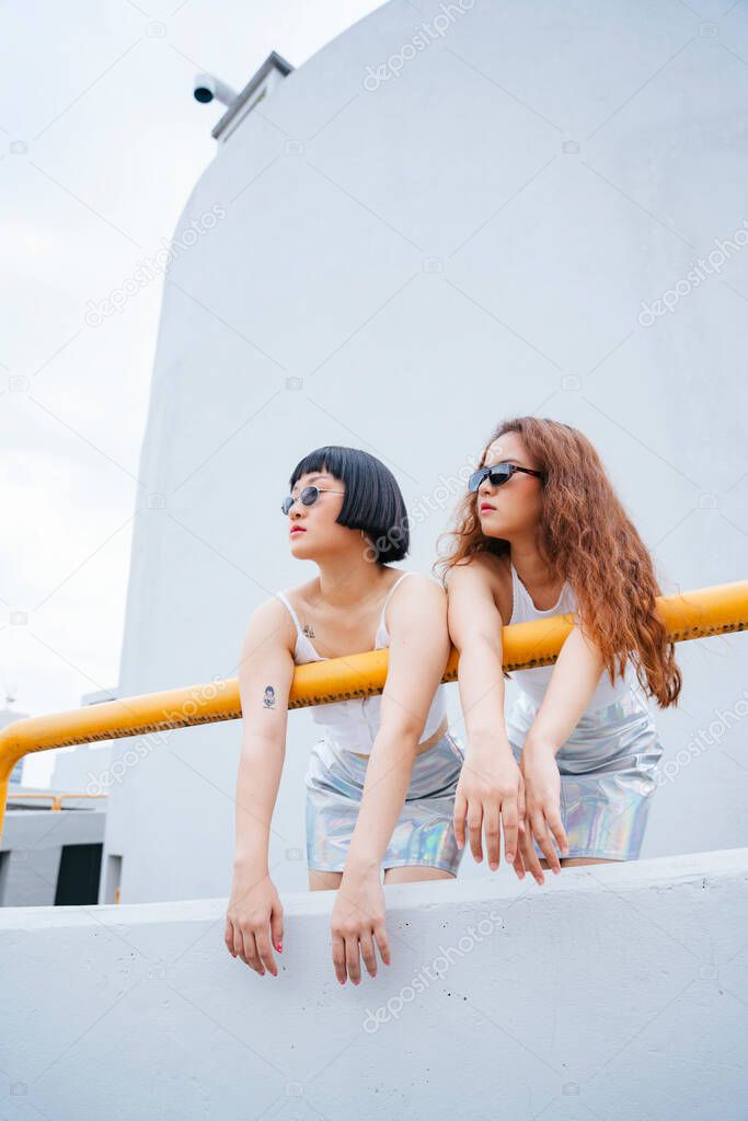 Portrait of two young asian women wear white vest and sunglasses at balcony.