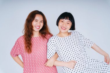 Beyaz ve pembe palkadot giymiş iki Asyalı kadının portresi el ele dans ediyor..