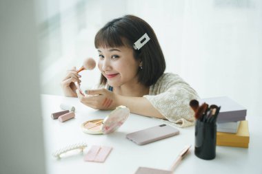 Güzel, güzel, genç Asyalı Taylandlı kadın beyaz odada kozmetik fırça aletleri kullanmaktan hoşlanıyor..