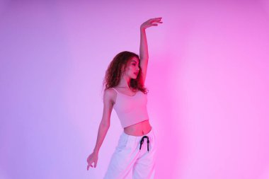 Aktif Asyalı kıvırcık saçlı kız stüdyoda neon ışıkta dans ediyor..
