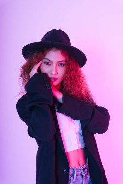 Asyalı kıvırcık saçlı bir kadının moda portresi siyah ceket giyer ve beyaz arka planda izole şapka takar..