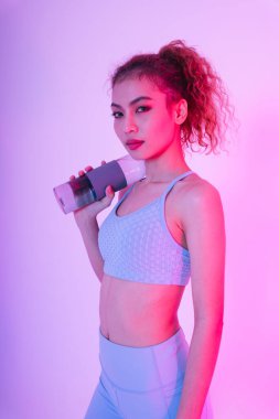 Pembe arka planda su şişesi olan sağlıklı kıvırcık saçlı genç Asyalı kadının portresi..