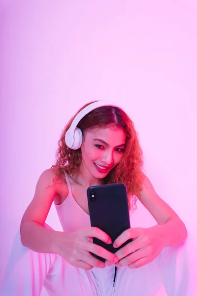 Young asian woman curly hairstyle listen to music with headphone and streaming on smartphone.