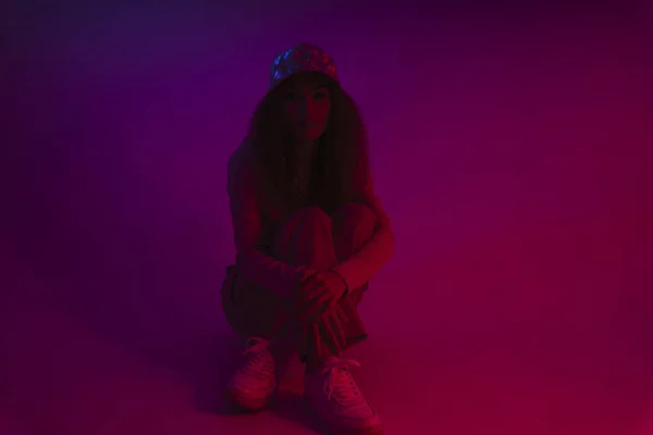 Genç Asyalı Kadın Neon Işıklı Arka Planda Yerde Oturan Şapka — Stok fotoğraf
