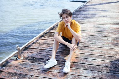 Sarı tişörtlü ve mavi pantolonlu bir adamın göldeki balkonda takıldığı yüksek açılı bir fotoğraf..