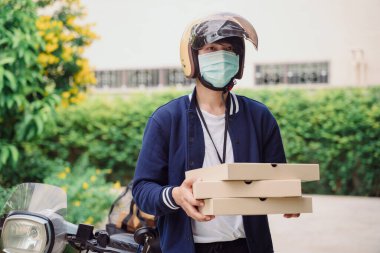 Pizza teslimatçısı maske takmış açık havada pizza kutusu tutuyor. Covid-19 salgını.