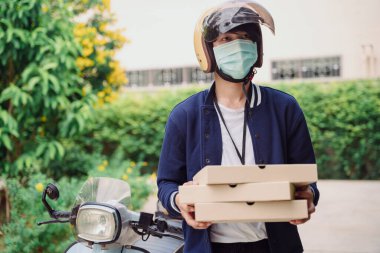 Pizza teslimatçısı maske takmış açık havada pizza kutusu tutuyor. Covid-19 salgını.