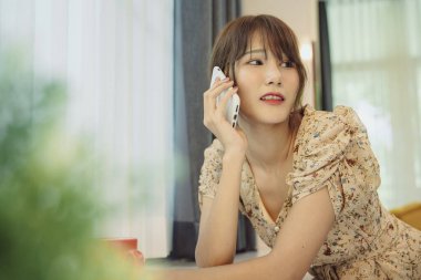 Güzel Asyalı Taylandlı kadın evde internet hizmeti için akıllı telefon kullanıyor..