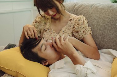 Romantik bir sahne. Asyalı Taylandlı çift oturma odasında. Kanepede kadın kucağında uzanan adam.