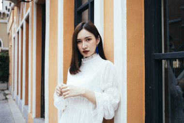 Kahverengi binaya yaslanmış beyaz elbiseli güzel, uzun saçlı kız..