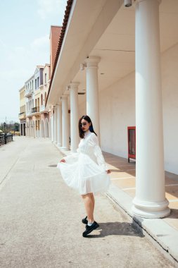 Güzel, uzun saçlı, beyaz elbiseli bir kız klasik şehirde rüzgarlı bir günde yürüyor..