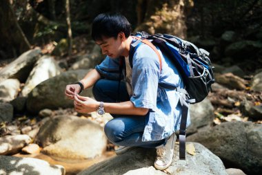 Erkek yürüyüşçü bir anlığına dinlenmek için kayanın üzerinde oturuyor..