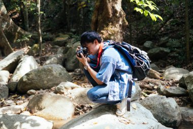 Erkek yürüyüşçü kayanın üzerinde oturuyor, gerisini çekmek ve kayanın fotoğrafını çekmek için..