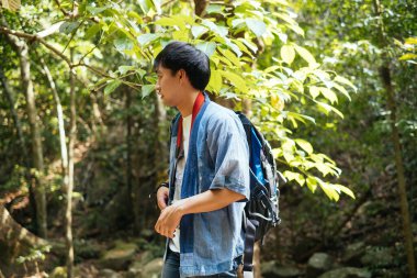 Erkek yürüyüşçü, ormanda bir kayanın üzerinde yürürken kuşların ve ağaçların fotoğrafını çeker..