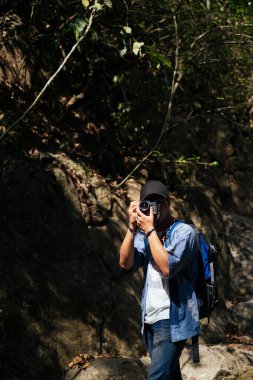 Erkek yürüyüşçü karanlık ormanda kamerayla yürür, doğanın fotoğrafını çeker..