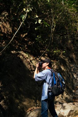 Erkek yürüyüşçü karanlık ormanda kamerayla yürür, doğanın fotoğrafını çeker..