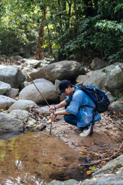 Erkek yürüyüşçü ormandaki büyük kayalarla şelalede dinleniyor..