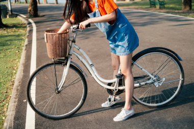 Parkta kadınların bacaklarının arasındaki beyaz bisikletin kırpılmış görüntüsü..