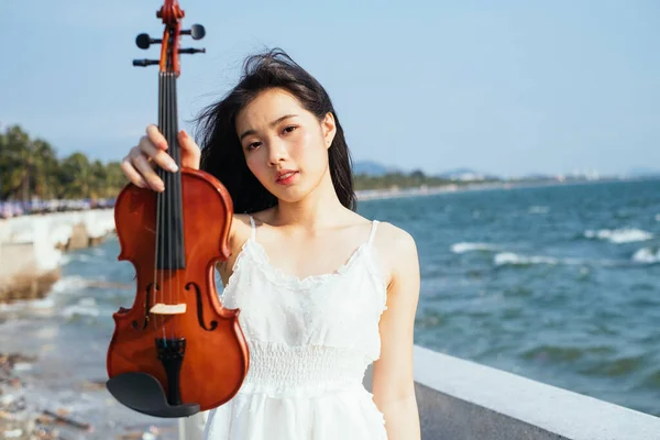 Black long hair woman show the violin to the camera at the sea in windy day.